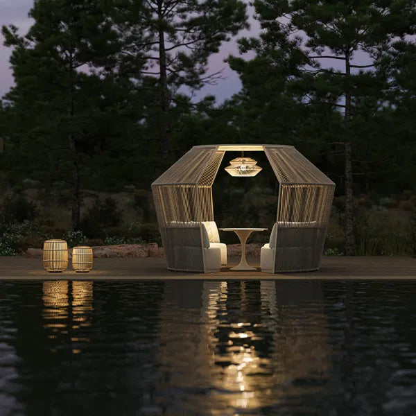 Modern outdoor seating pod with elegant lighting and a central table, surrounded by trees, reflecting on the water, creating a serene and inviting atmosphere for relaxation.