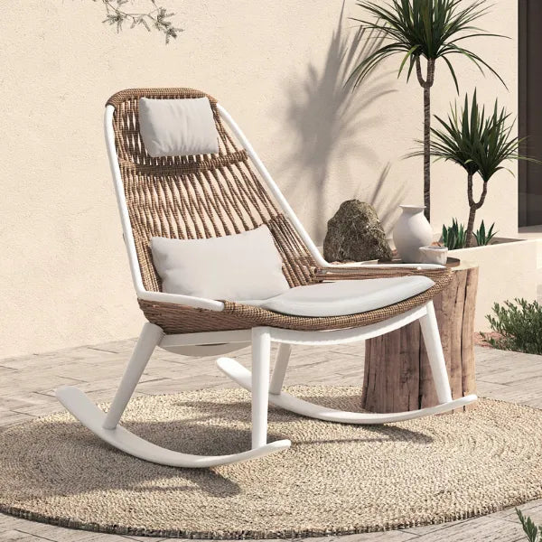 Modern rocking chair with a woven seat and sturdy white frame, placed on a circular outdoor rug surrounded by some greenery, perfect for outdoor relaxation.